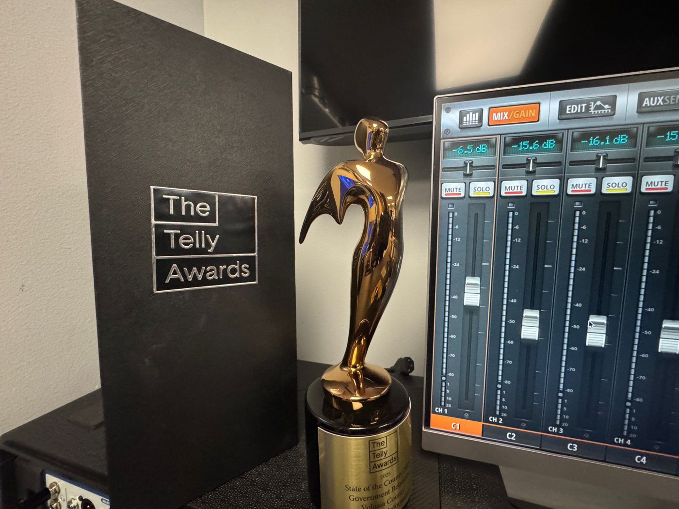A Telly Award trophy beside its presentation case and an audio mixing console